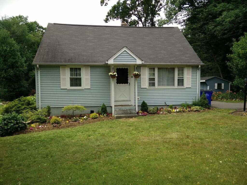 Before photo of a little blue house with vinyl siding and a small porch