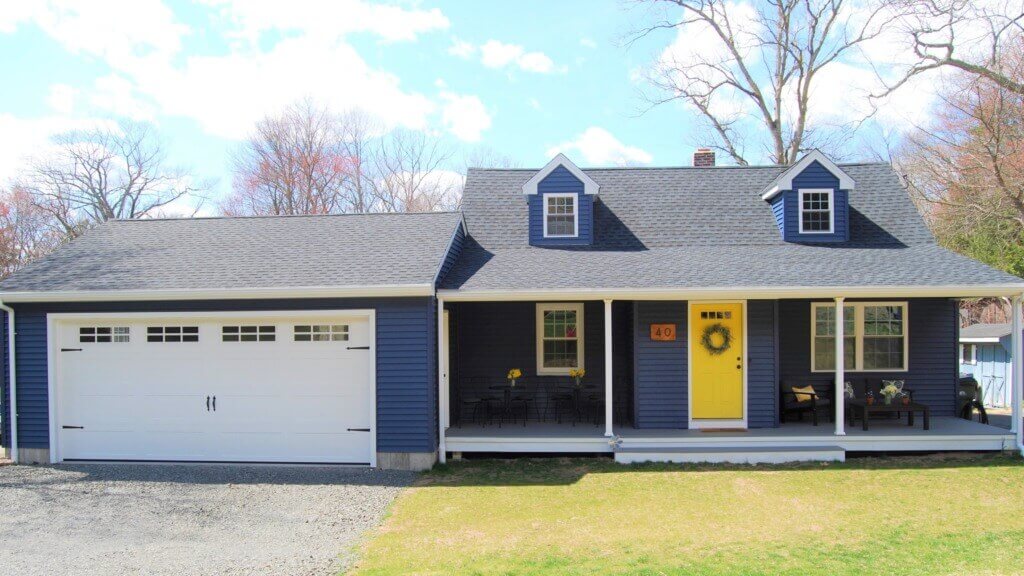 After photo of the same house repainted, with a wrap-around porch, dormer windows, and an attached garage.